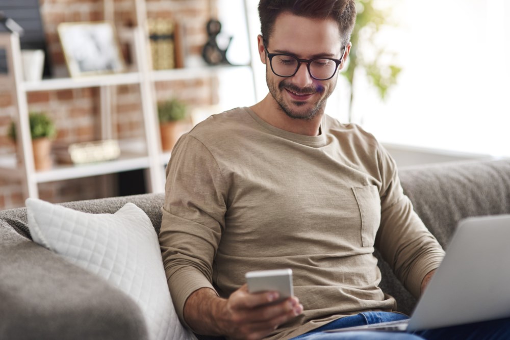 En mann som har pc-en sin i fanget mens han ser på telefonen sin