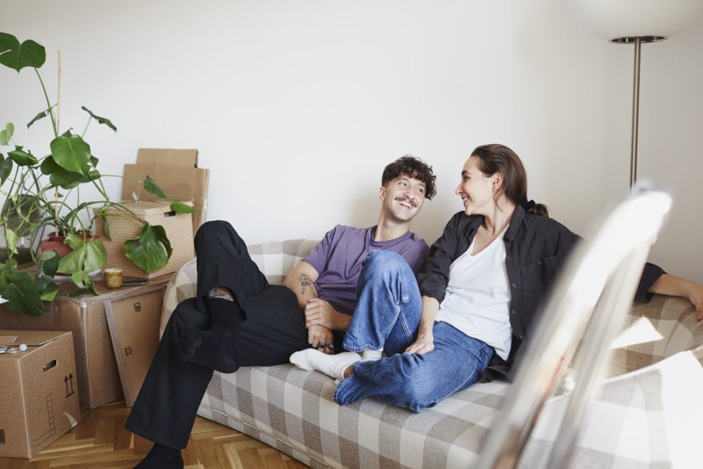 En mann og en kvinne sitter på sofaen omgitt av flytteesker