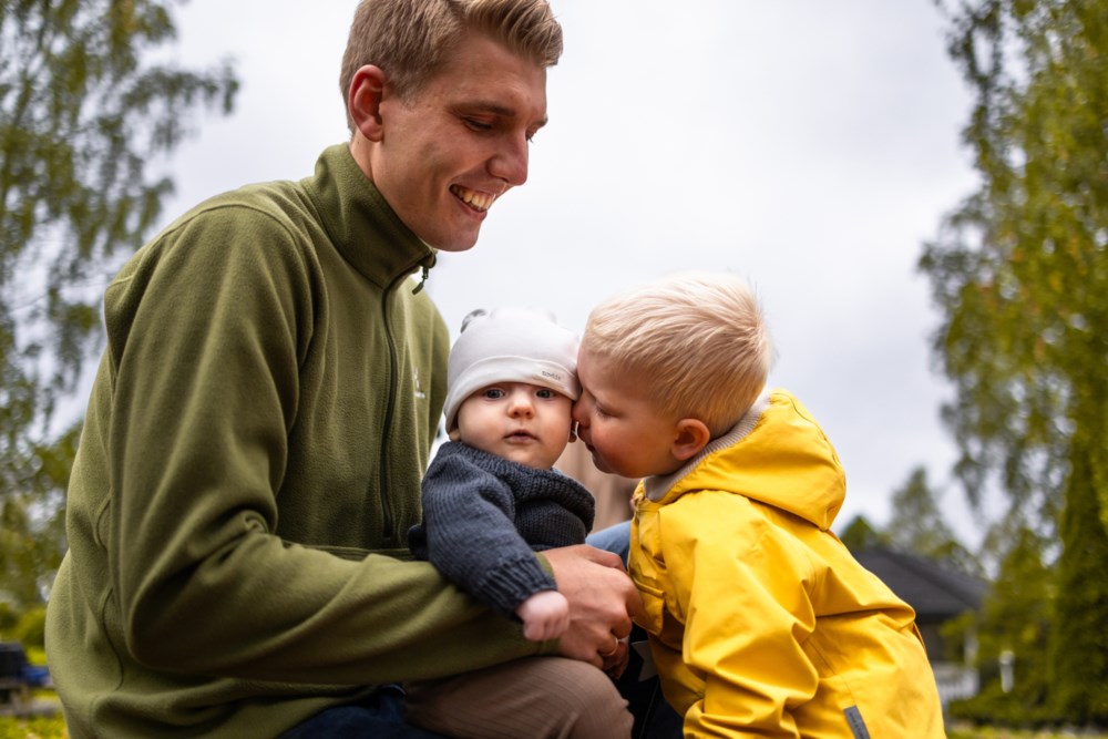 far med lillebror på fanget sitt og storebror gir han en klem