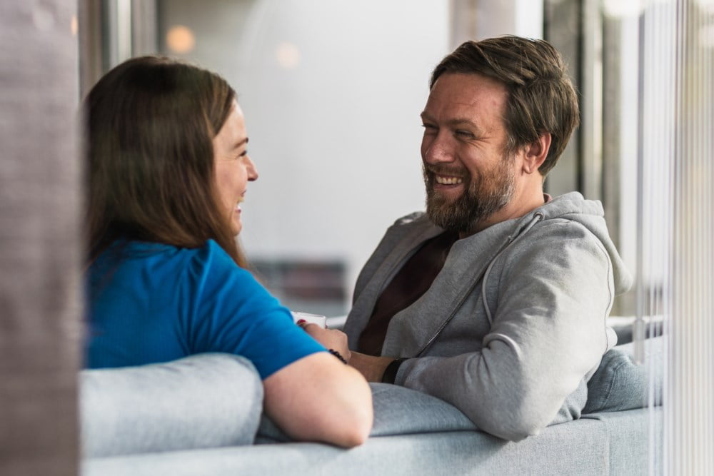 Ser inn gjennom vinduet på kvinne og mann i sofaen som smiler til hverandre