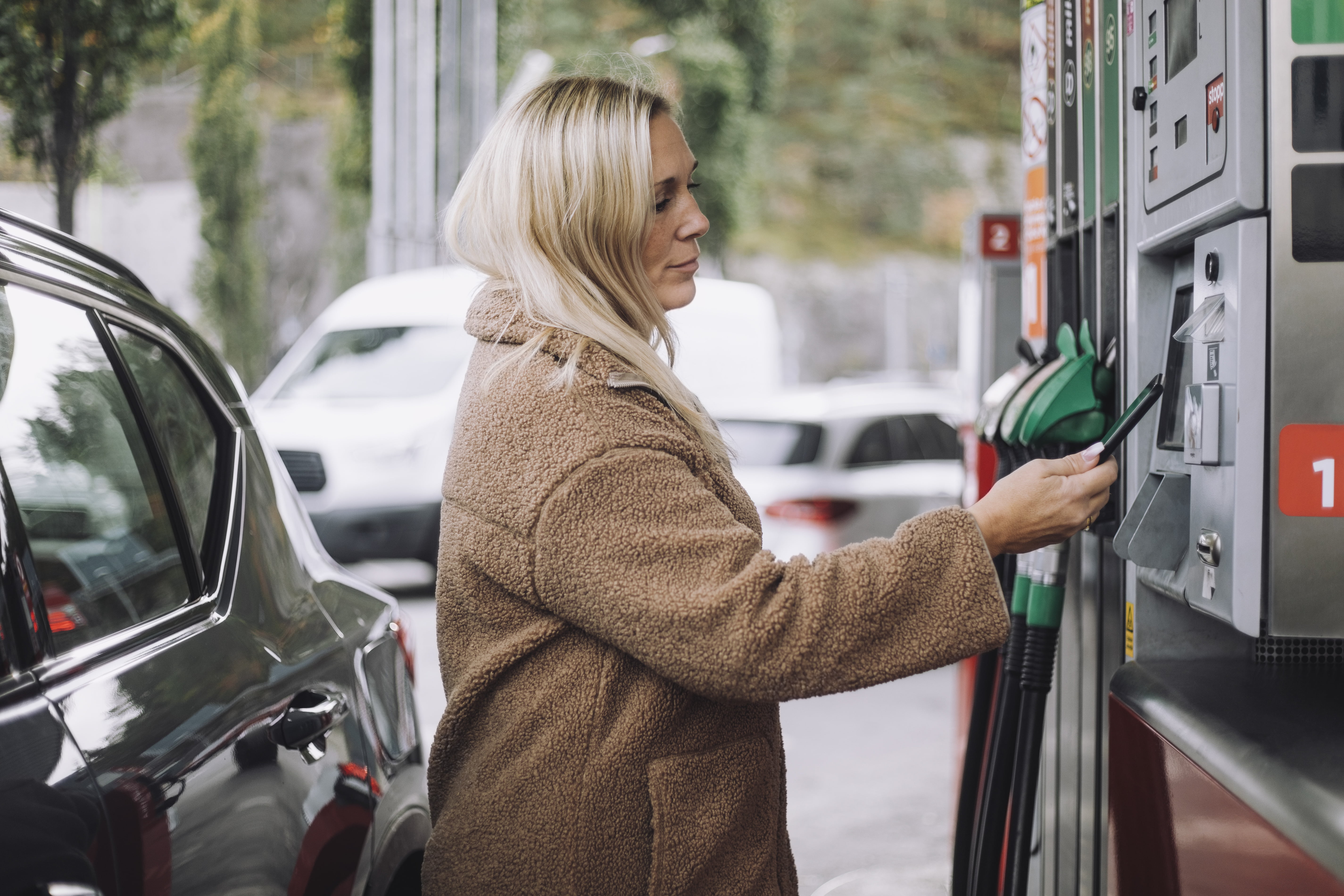 Dame som betaler med mobilen på bensinstasjon